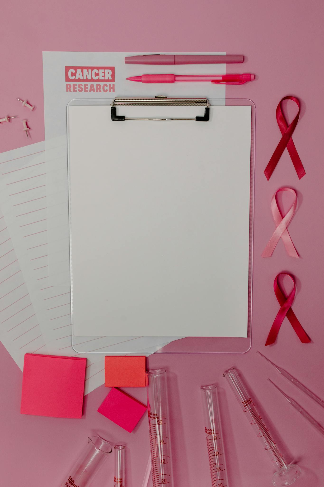 Clipboard with pink ribbons and cancer research papers on a pink background.