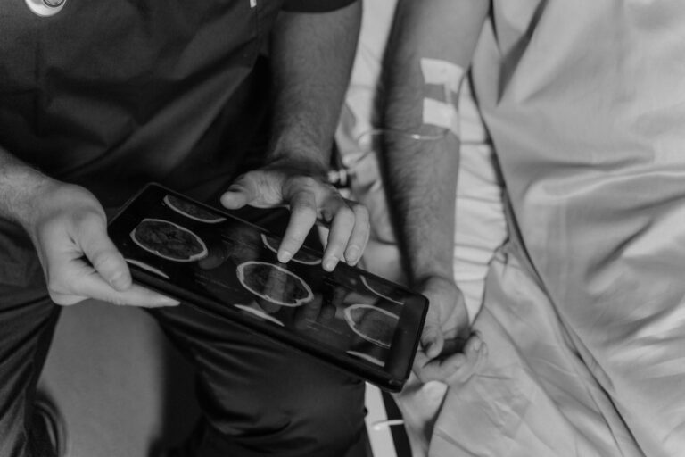 Medical professional reviews patient's CT scans on a digital tablet in grayscale.