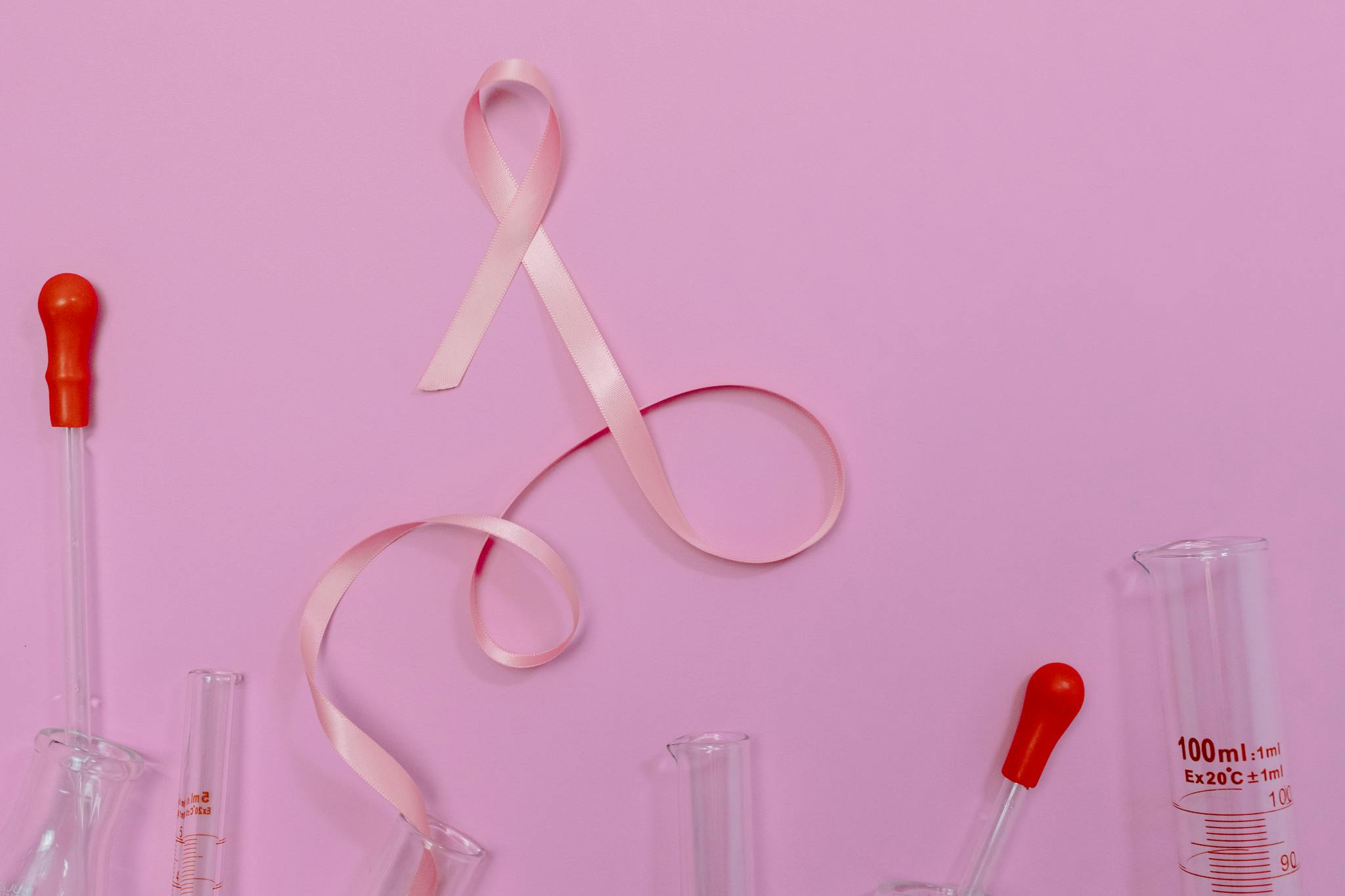 Pink ribbon symbolizing breast cancer awareness with laboratory glassware on a pink backdrop.