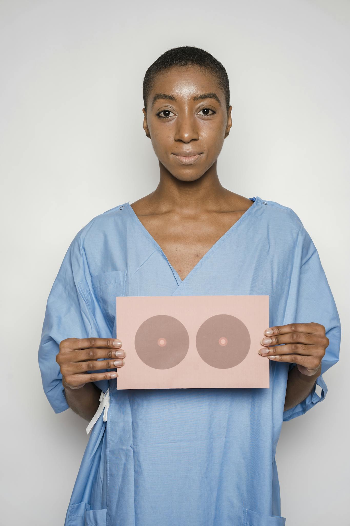Woman in medical gown holding breast cancer awareness card symbol, promoting health care education.